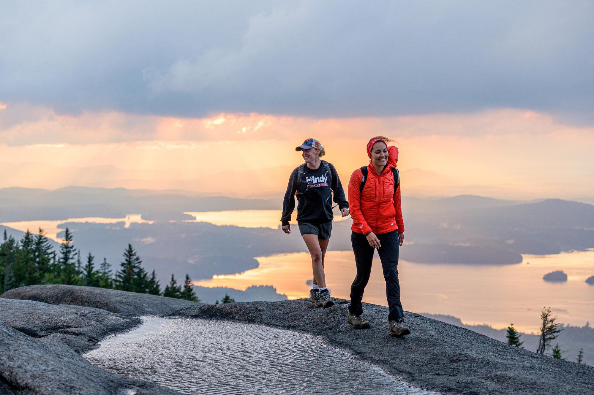 Hikers at the top of Ampersand Mountain with a hazy sunset as the backdrop