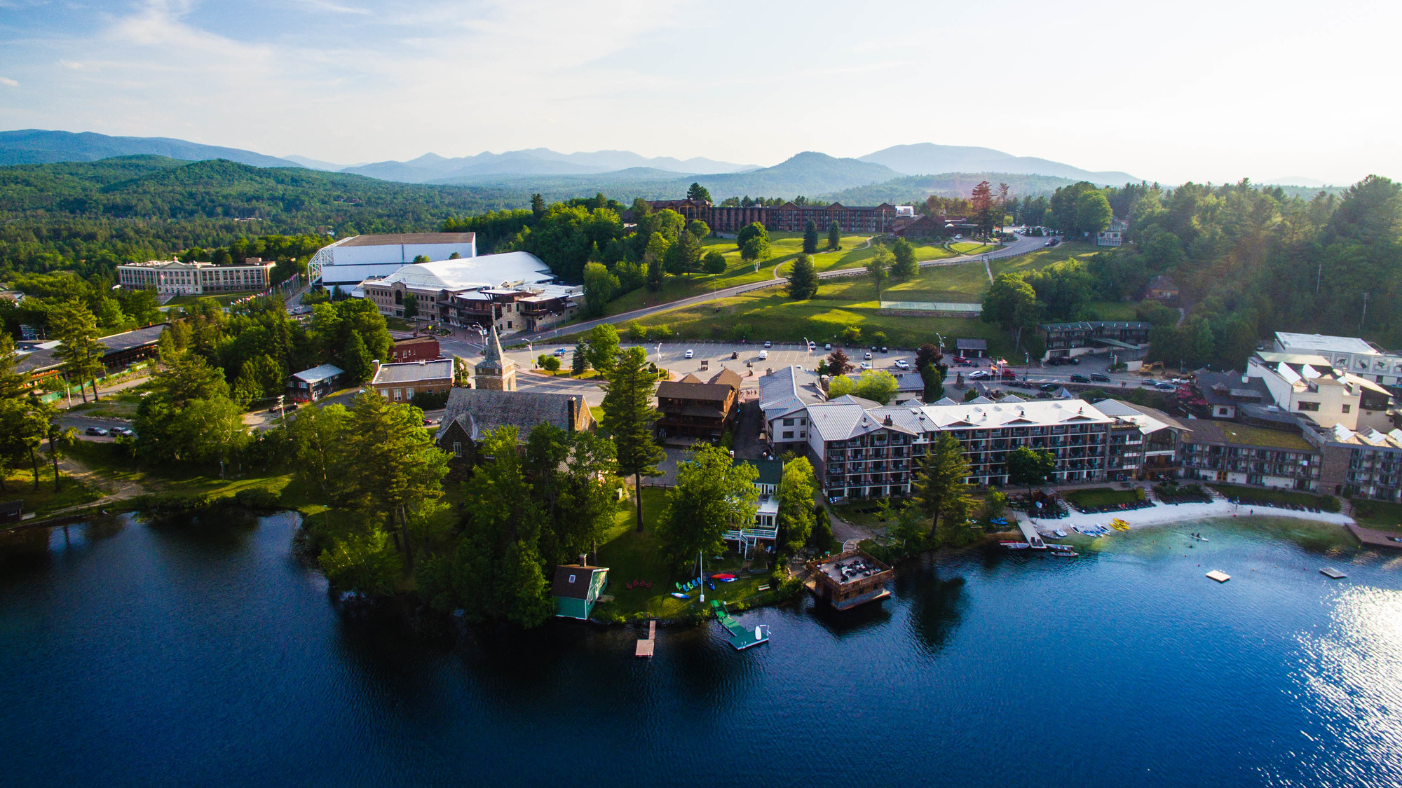 Village of Lake Placid, on the shore of Mirror Lake in summer with green trees, blue water and sunshine.