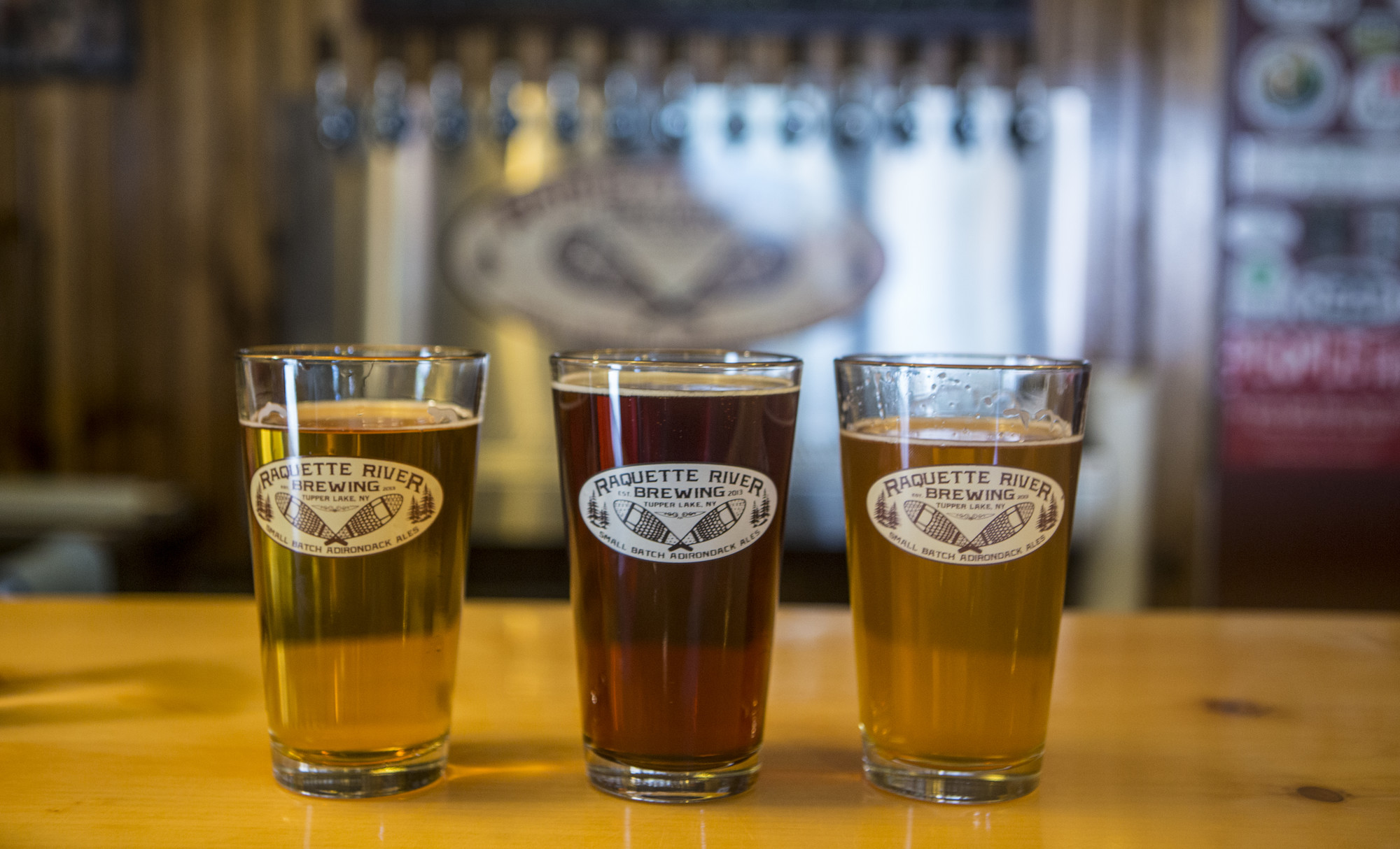 3 beers placed on a bar. The beer is golden, 2 lighter versions and a dark beer